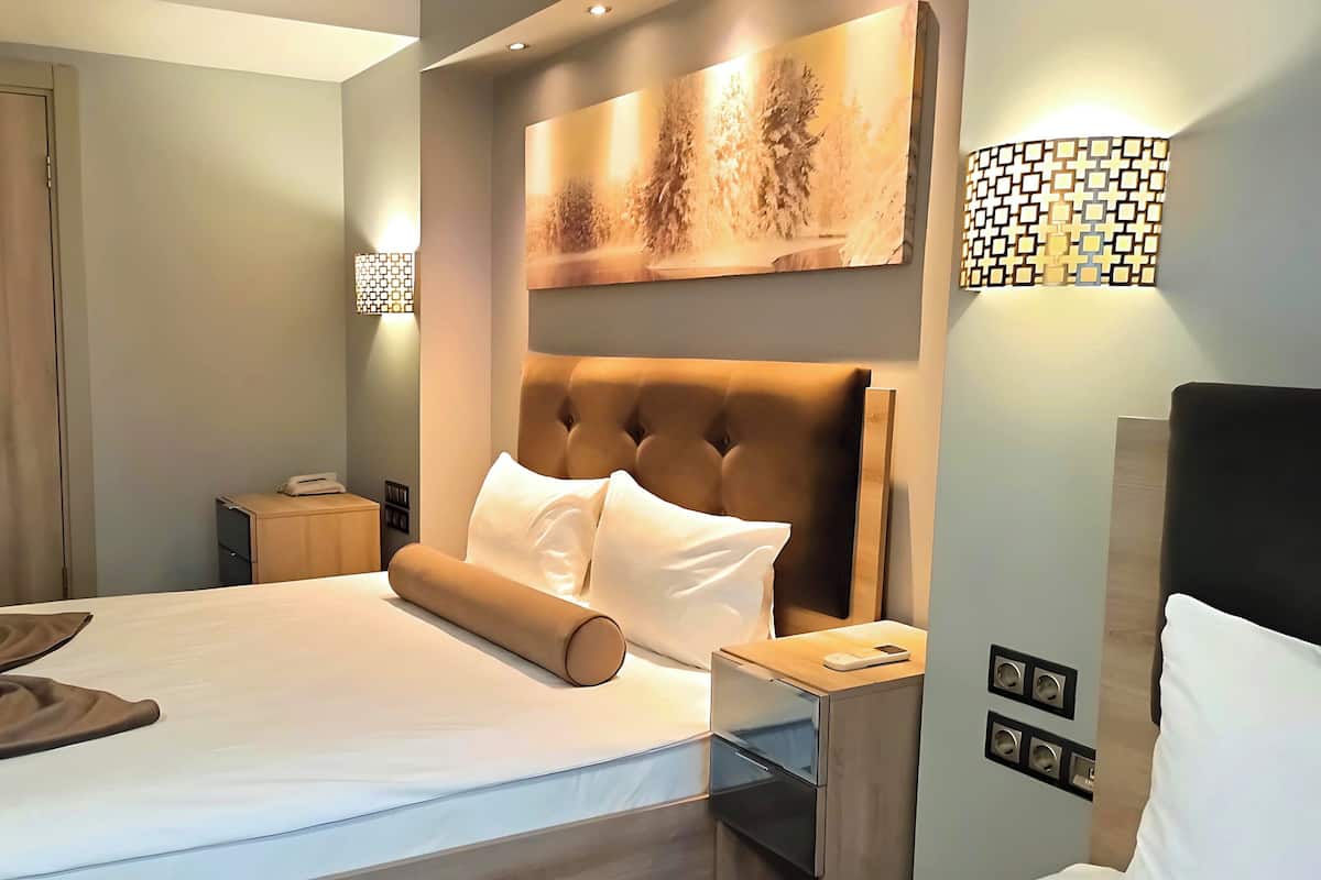 Une chambre d’hôtel avec un grand lit, une tête de lit, une table de chevet, une commode, une lampe fixée au mur et une porte.