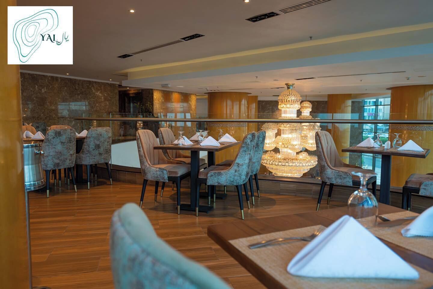 Un restaurante con una decoración moderna, que cuenta con una lámpara de araña, suelo de madera y sillas tapizadas.