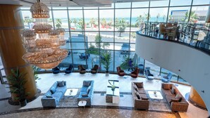 A spacious lobby with a large chandelier, comfortable seating, and a view of the beach through large windows. - Grand Hotel (Salmiya)