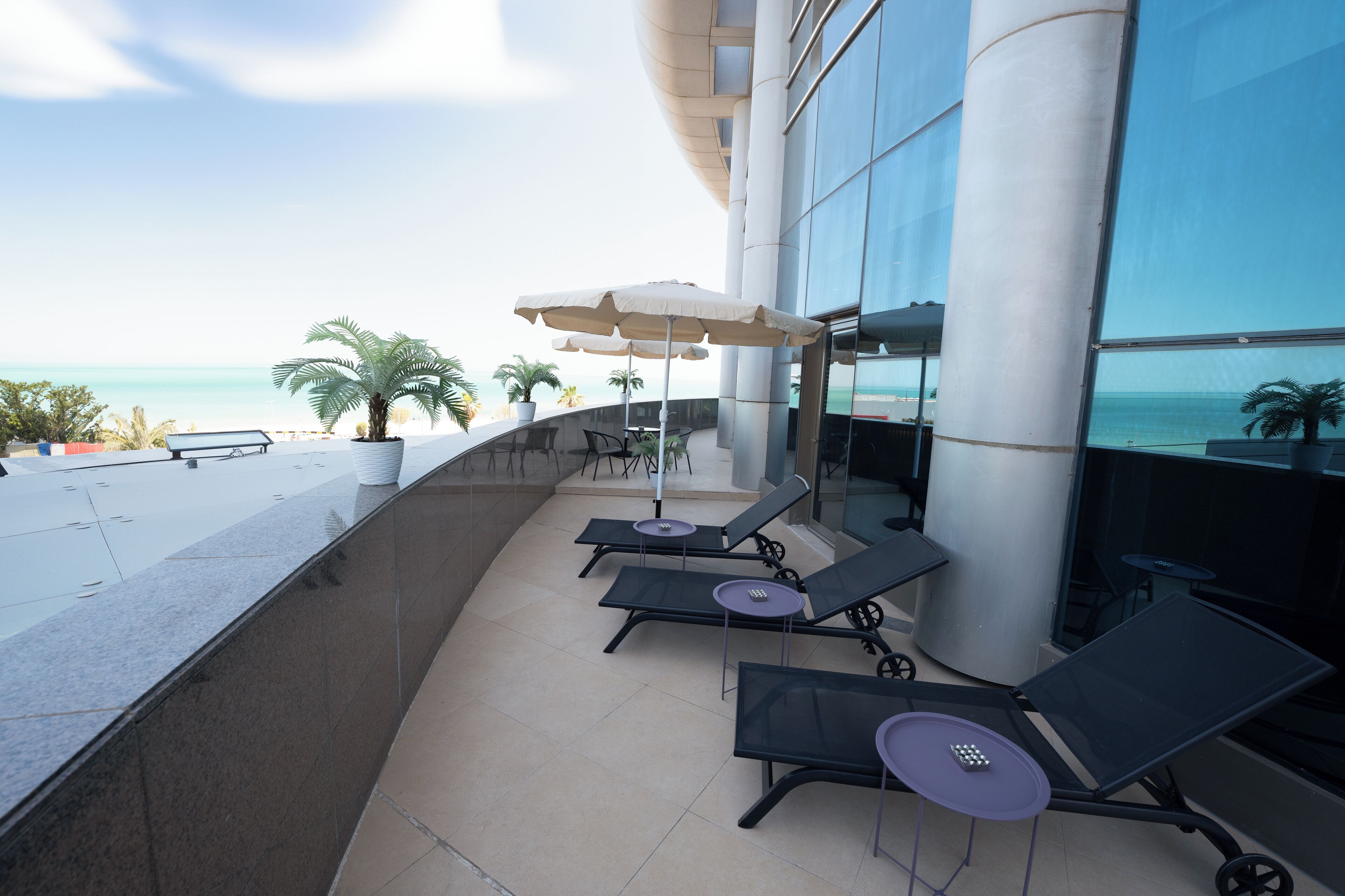 Een moderne buitenlounge met ligbedden en parasols, met uitzicht op een strand.