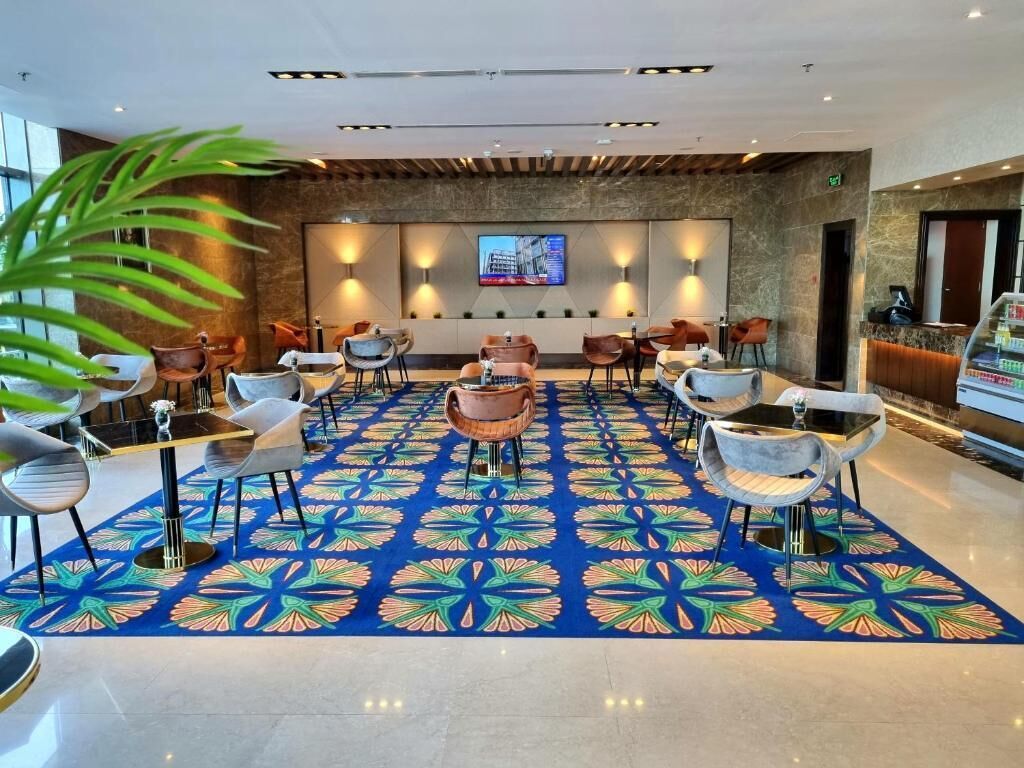 Un vestíbulo de hotel con alfombra estampada, varias zonas de estar y una pantalla de televisión en la pared.