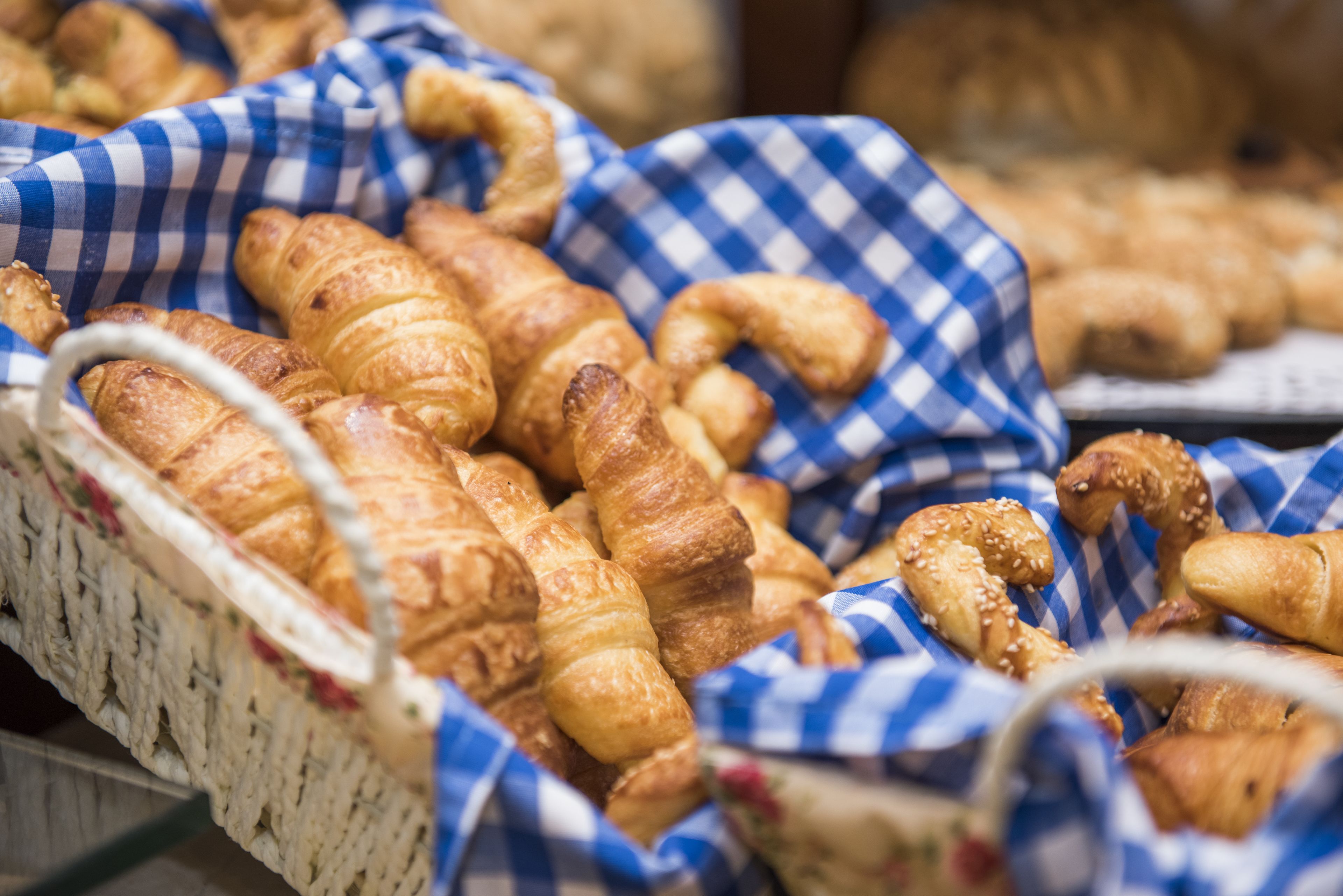 A basket filled with various types of croissants and pastries, arranged on a checkered cloth.