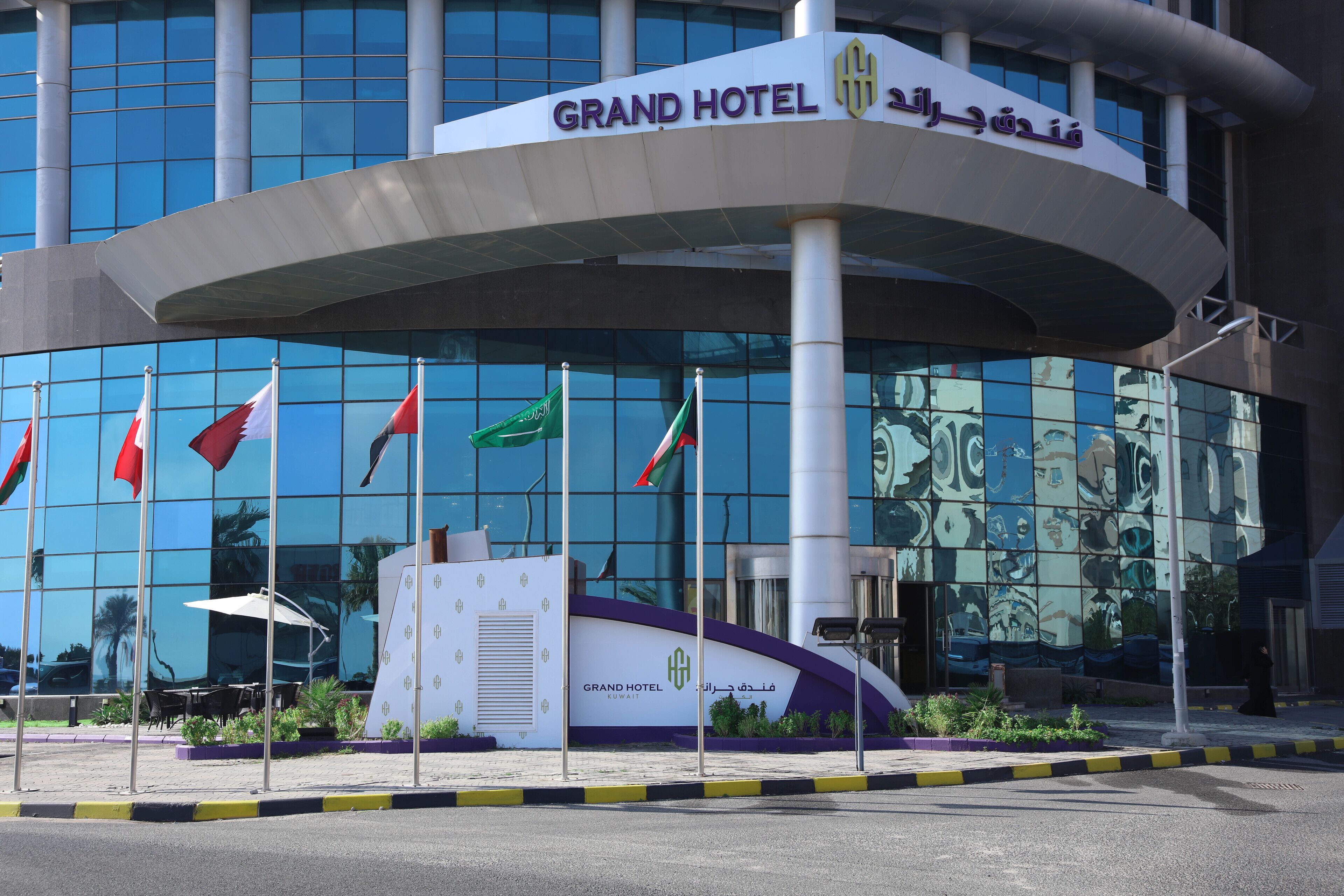 A modern Grand Hotel building with a curved entrance, multiple flags, and a glass facade reflecting the surroundings.
