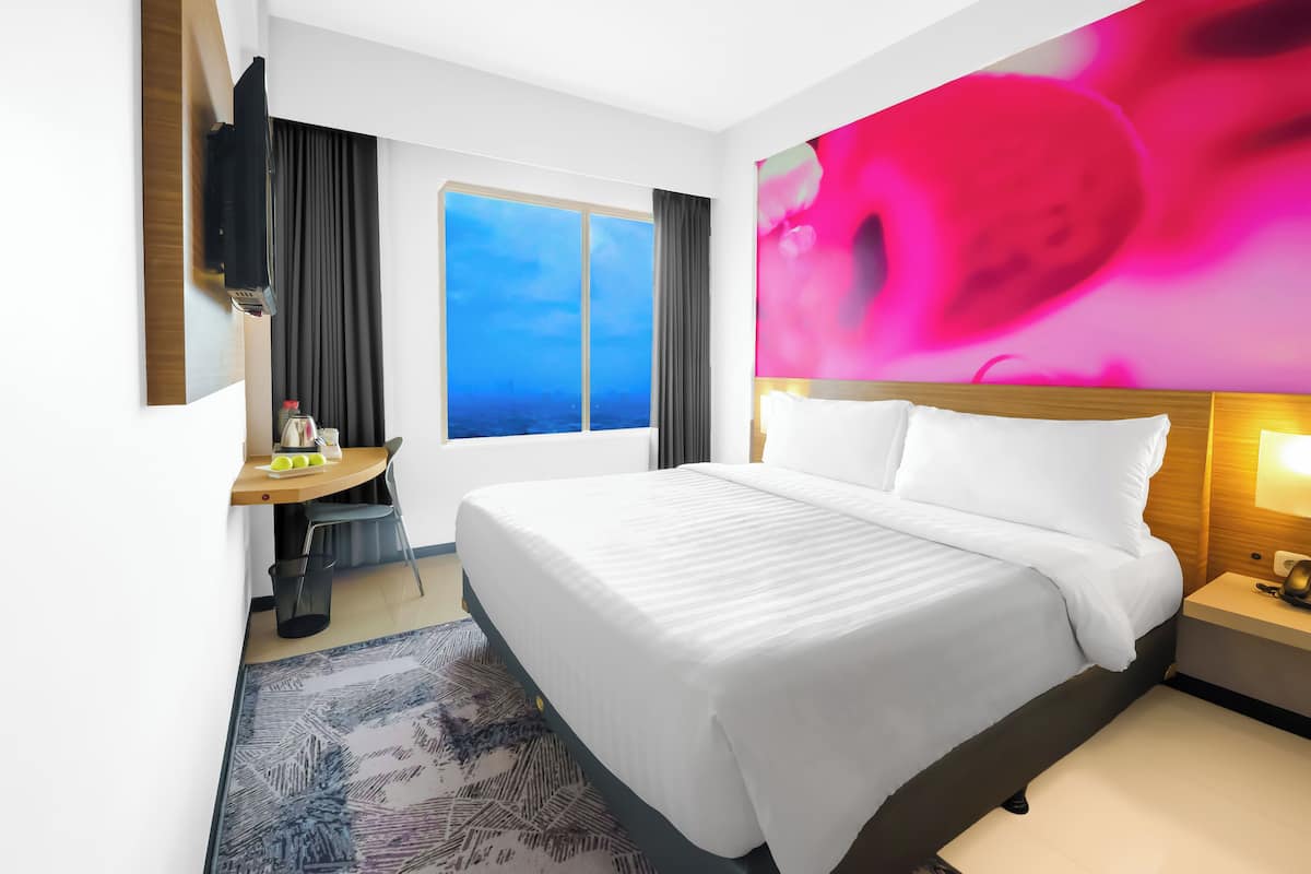 Hotellihuone, jossa on suuri sänky, työpöytä tuolilla, seinälle asennettu televisio, ikkuna, josta on näkymä, ja yöpöytä lampulla.