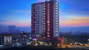 Un grand hôtel à plusieurs étages, avec une façade rouge et blanche bien visible, et un parking situé à l’avant.