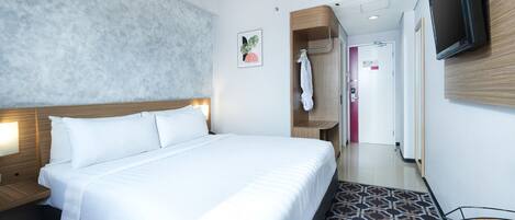 Habitación de hotel con cama, televisión montada en la pared, equipo de aire acondicionado, perchero y piso estampado.