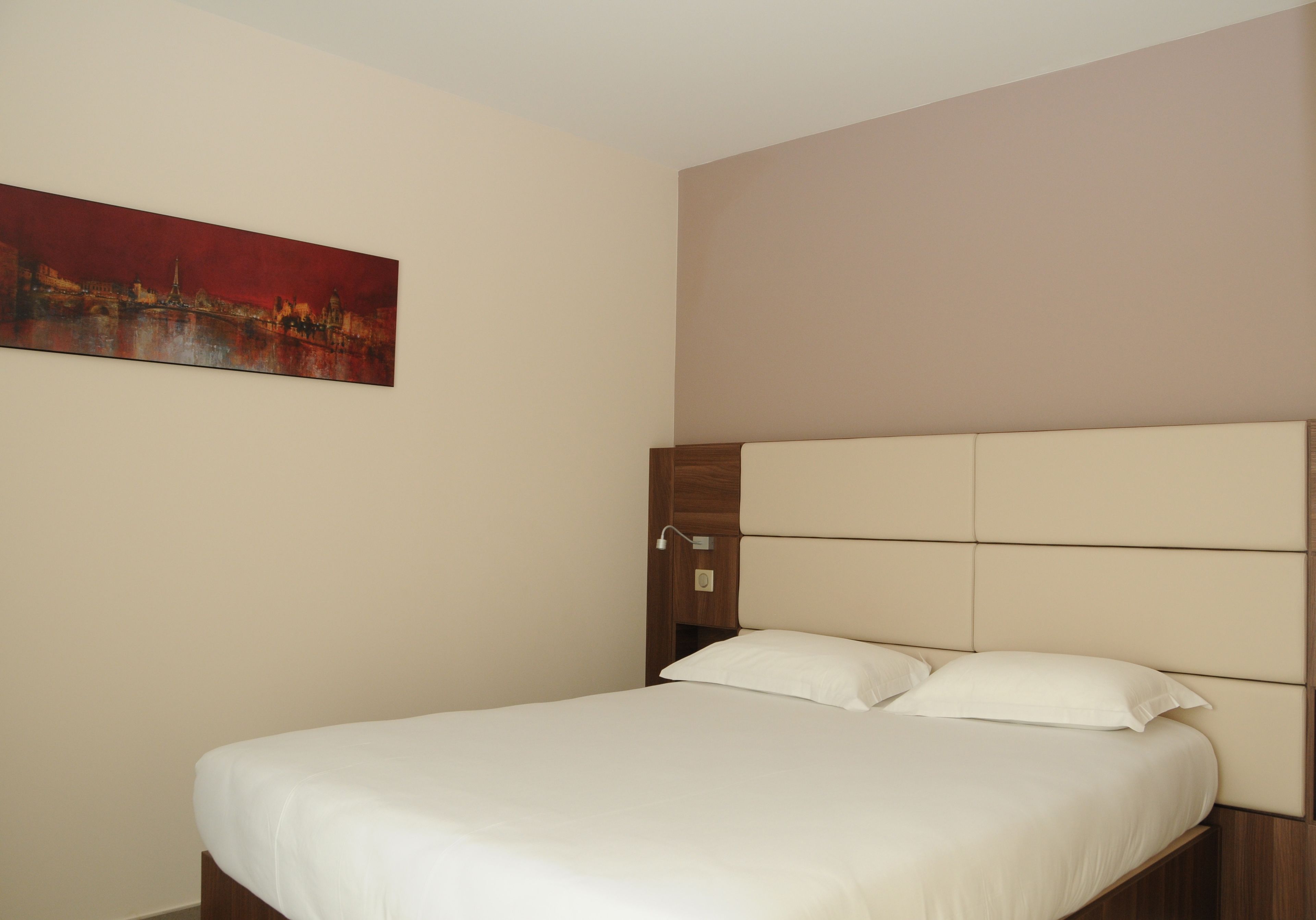 A hotel room with a bed, a headboard, and a painting on the wall.