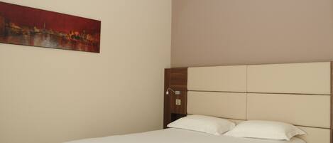 A hotel room with a bed, a headboard, and a painting on the wall.