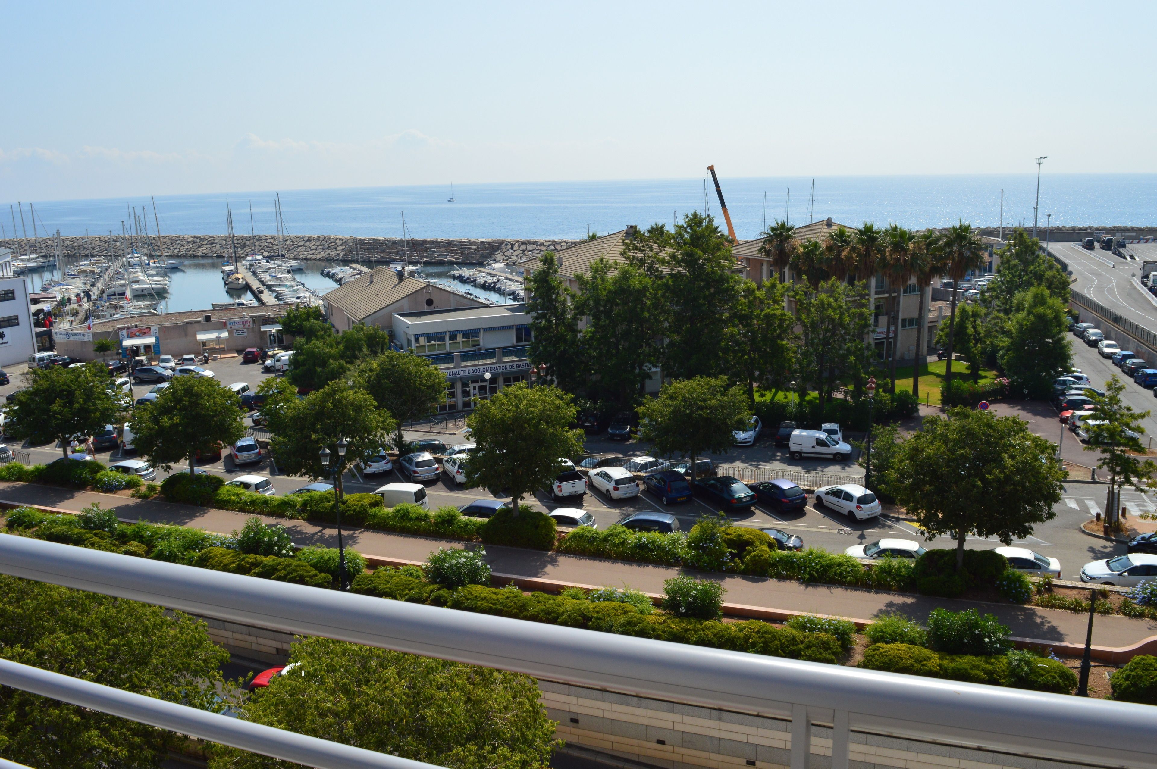 A coastal marina with boats, a parking lot, and buildings with balconies overlooking the sea.