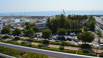A coastal marina with boats, a parking lot, and buildings with balconies overlooking the sea.