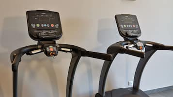 Two treadmills with digital displays, a wall socket, and a framed picture on the wall.