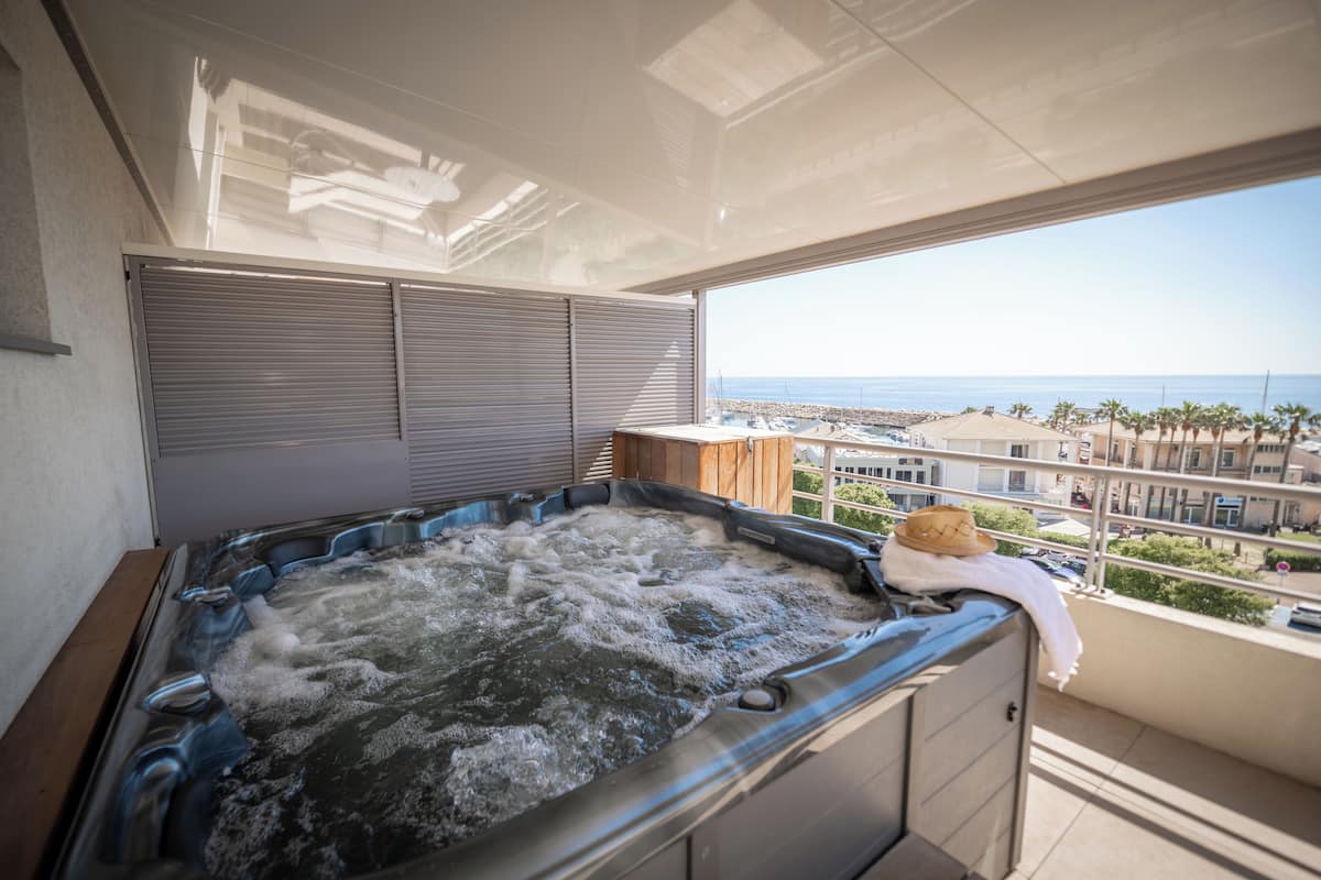 Uma banheira de hidromassagem em uma varanda com vista para o mar e edifícios.