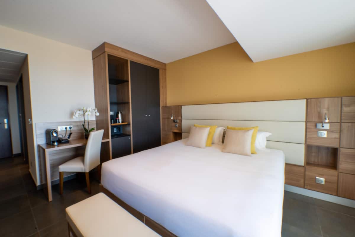 Quarto de hotel moderno com uma cama grande, uma escrivaninha com cadeira e armários embutidos.