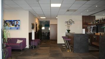 Un vestíbulo de hotel moderno con recepción, zona de bar, asientos morados y un comedor al fondo.