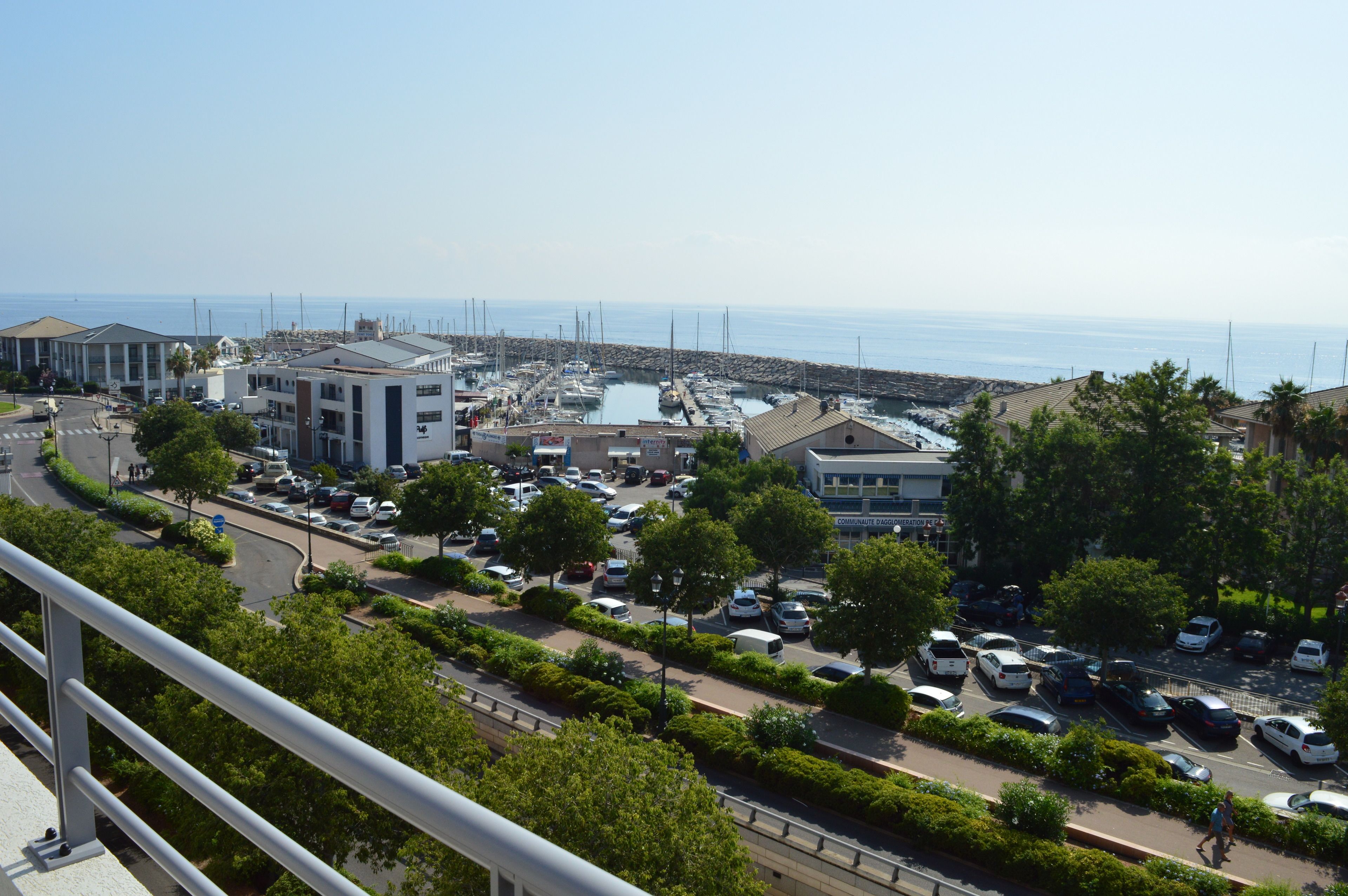 Un puerto costero con barcos, una zona de estacionamiento y edificios con balcones que dan al mar.