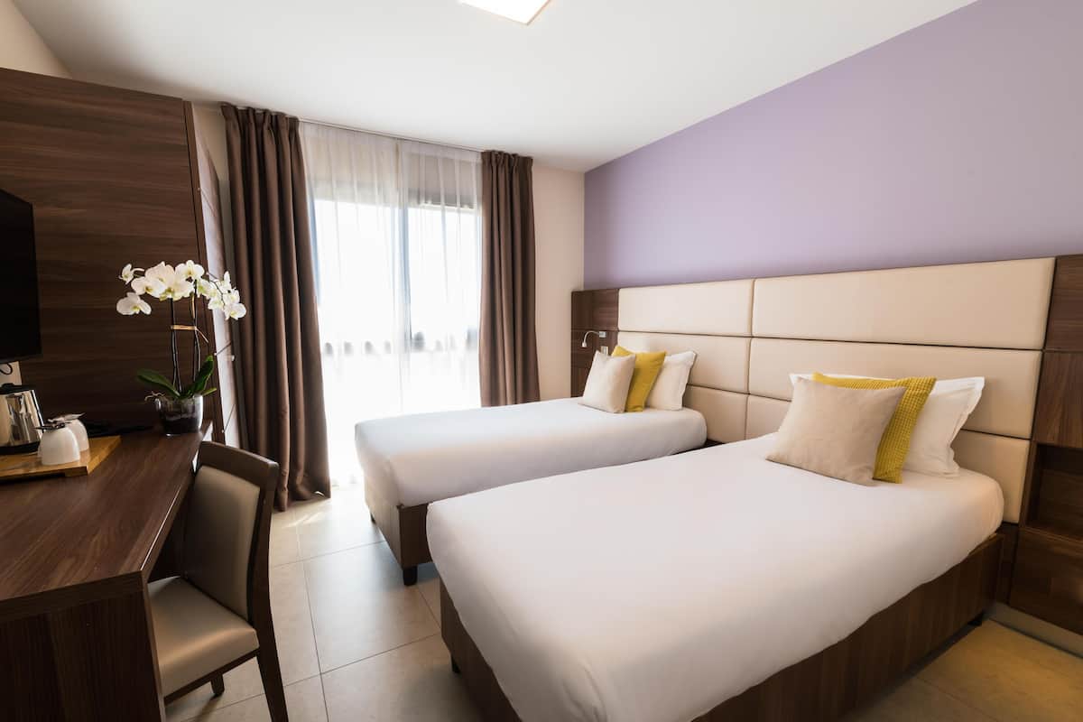Quarto de hotel com duas camas, uma mesa e uma televisão.