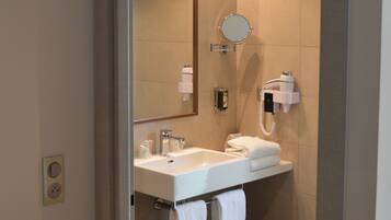 A modern bathroom with a white sink, a mirror, a handheld hair dryer, and a bench.