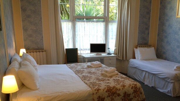 Une chambre d’hôtel avec un grand lit, un plus petit lit, un bureau avec un ordinateur et une fenêtre avec des rideaux.