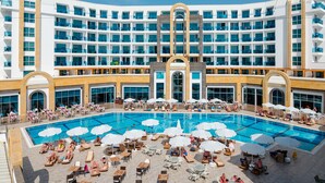Ett stort hotell med en central pool som omges av solstolar och parasoller.