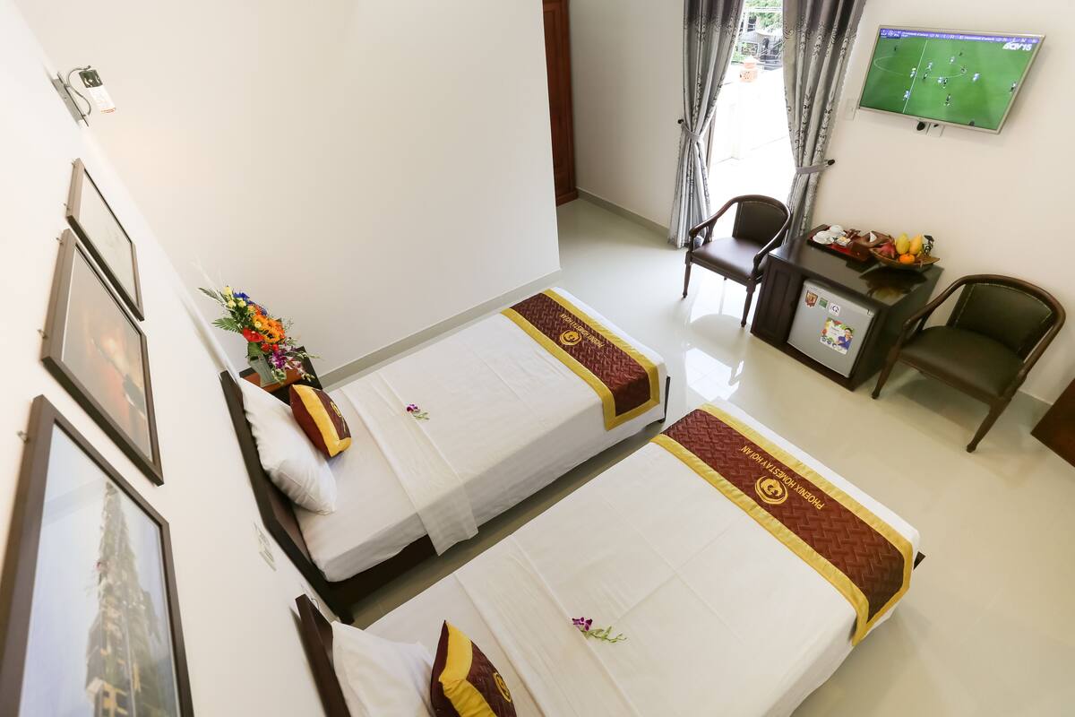 A hotel room with two beds, a desk with a television, and framed pictures on the wall.