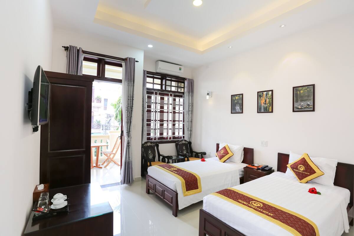 A hotel room with two beds, a desk, a chair, and a window with curtains.