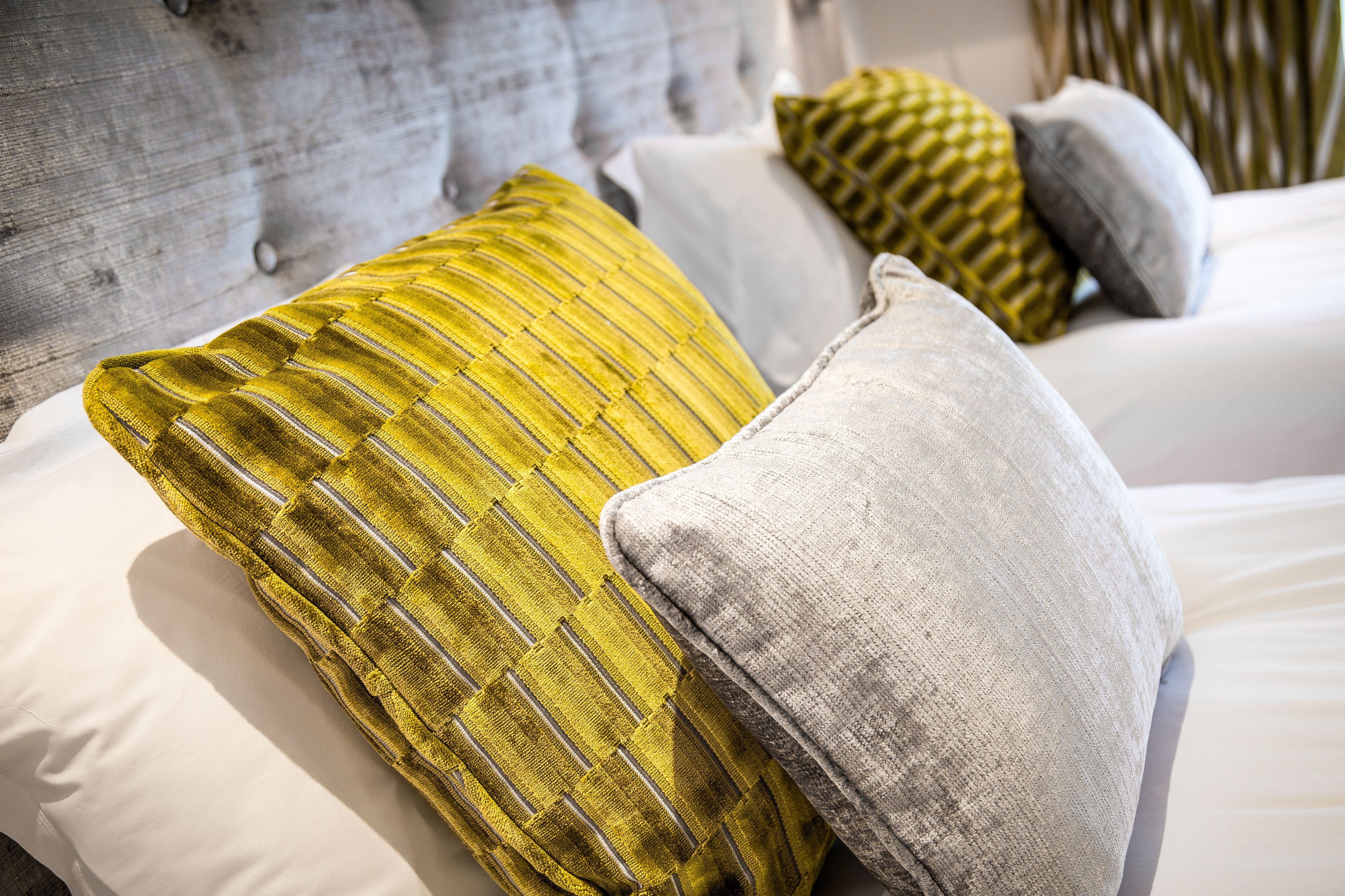 Un lit doté d’une tête de lit rembourrée de couleur grise, de draps blancs et d’oreillers décoratifs aux tons jaune et gris.