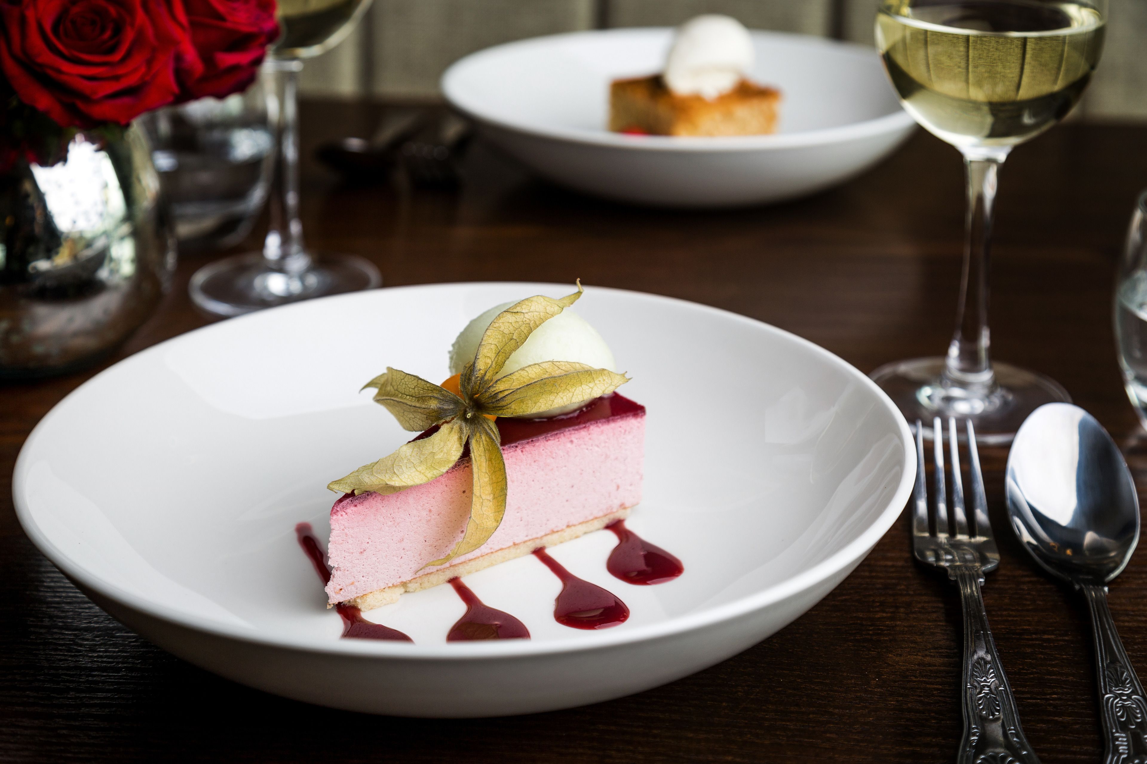 Un postre sobre un plato blanco, acompañado de una hoja decorativa, un tenedor y una cuchara sobre una mesa de madera.