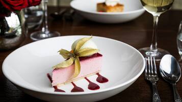 Un postre sobre un plato blanco, acompañado de una hoja decorativa, un tenedor y una cuchara sobre una mesa de madera.