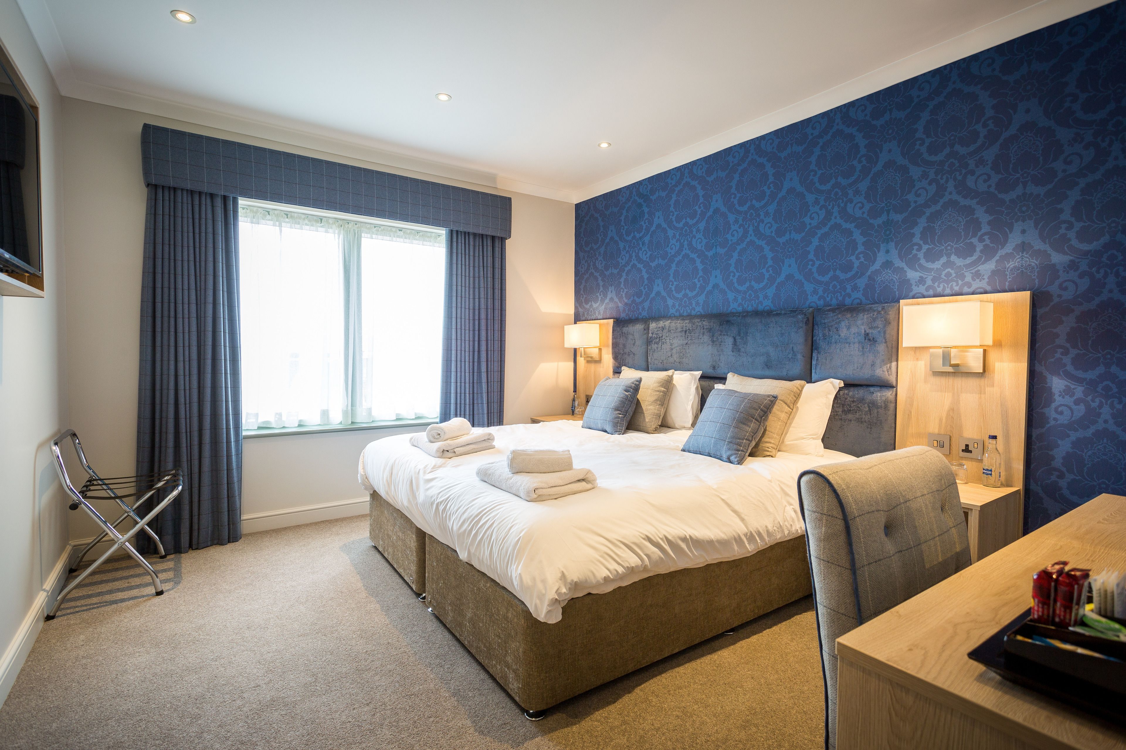 A modern hotel room with a large bed, a desk, and a window with curtains.