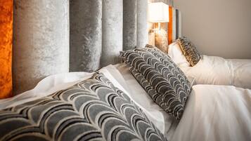 A modern hotel room with a large bed, multiple pillows, a nightstand with a lamp, and a patterned wallpaper.