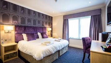 A hotel room with a large bed, a desk, a chair, a nightstand, and a wall mural.