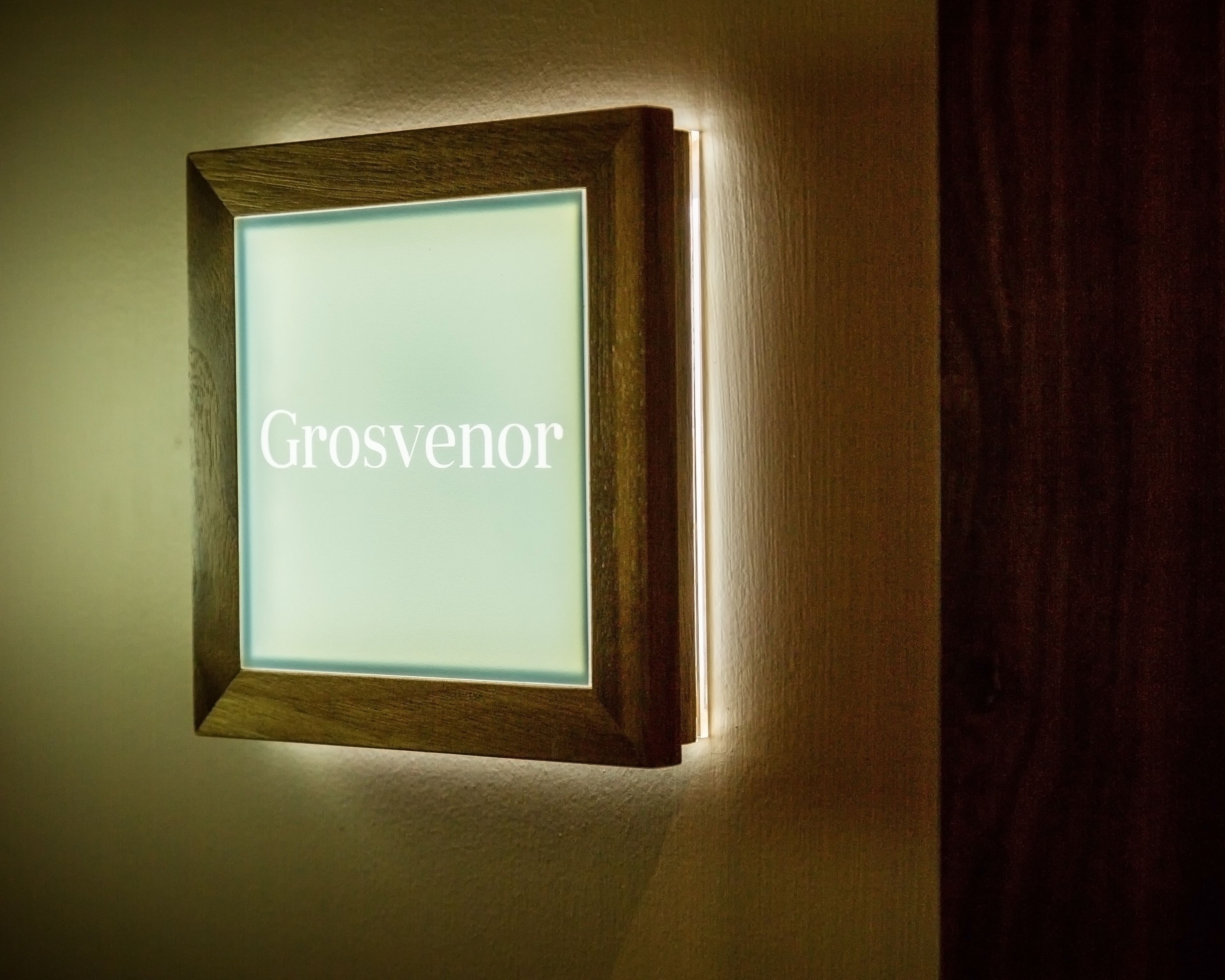 A framed sign with the word "Grosvenor" illuminated against a wall.