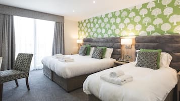 Quarto de hotel com duas camas, uma cadeira e uma janela grande com cortinas.