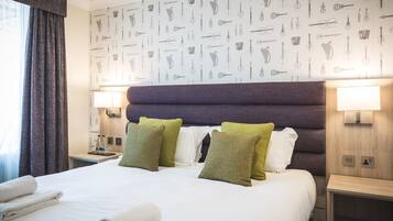 Habitación de hotel con una cama grande, dos almohadas, cabecera, lámparas de noche y una pared con motivos de instrumentos musicales.