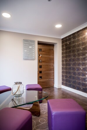 A reception area with a glass table, purple seating, a directional sign, and a wooden door. - The Nottinghamshire Hotel and Golf Club (Nottingham)