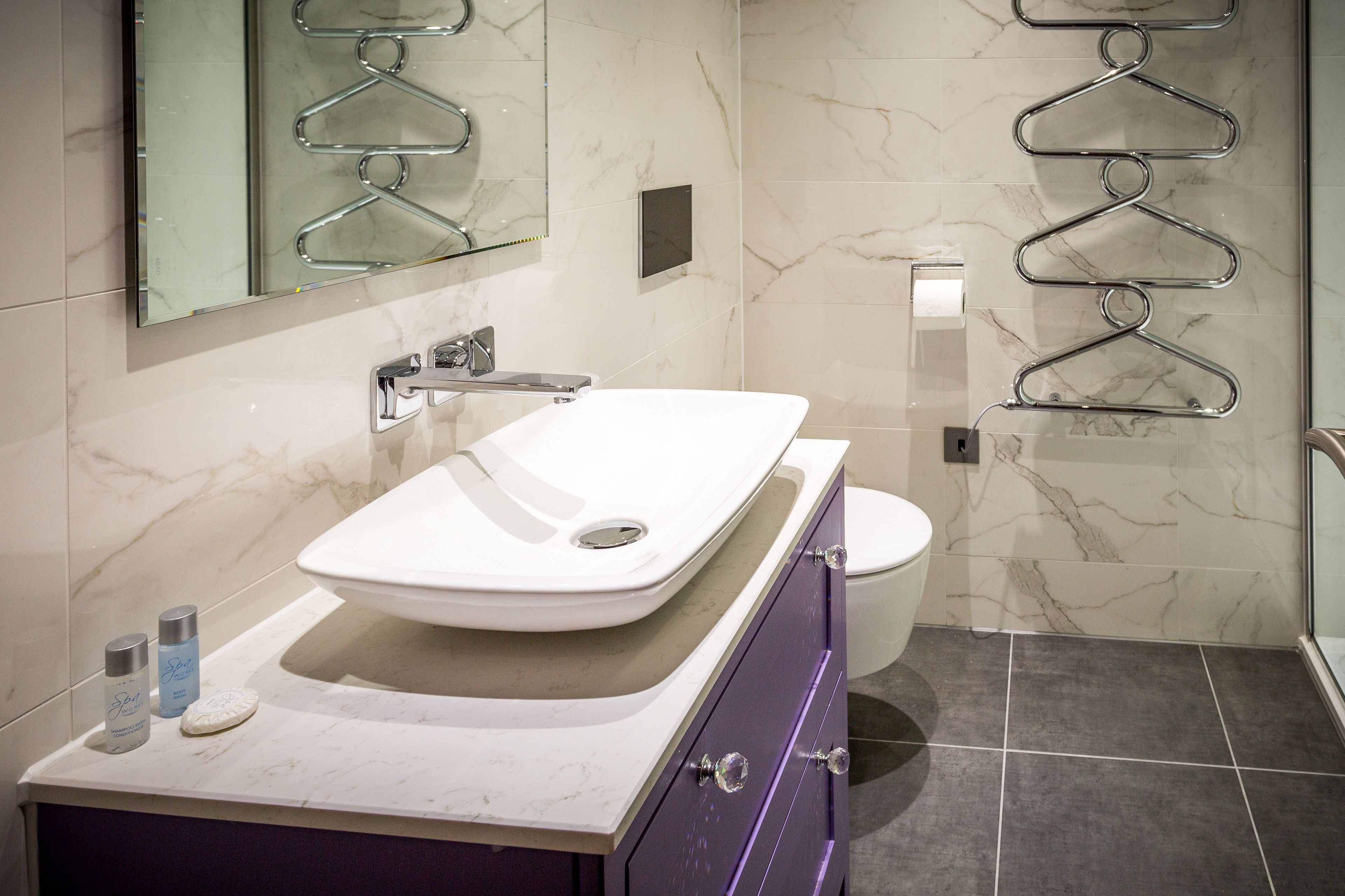 A bathroom with a white sink, a toilet, and a mirror. There are two bottles on the sink counter.