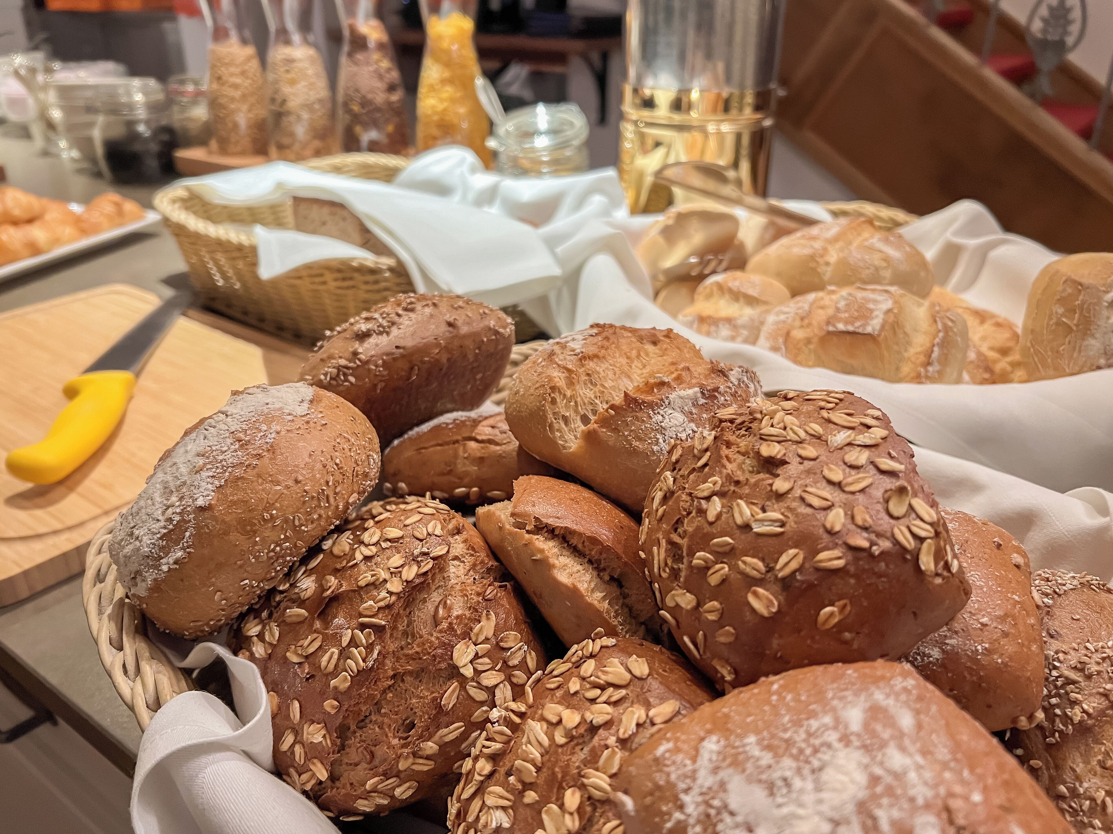 A variety of breads and pastries on display, including loaves with sesame seeds and a basket of croissants.
