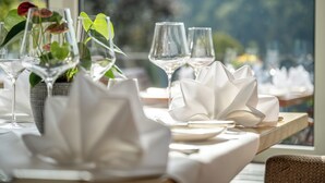 Una mesa de comedor preparada con servilletas blancas, copas de vino y un florero con flores.