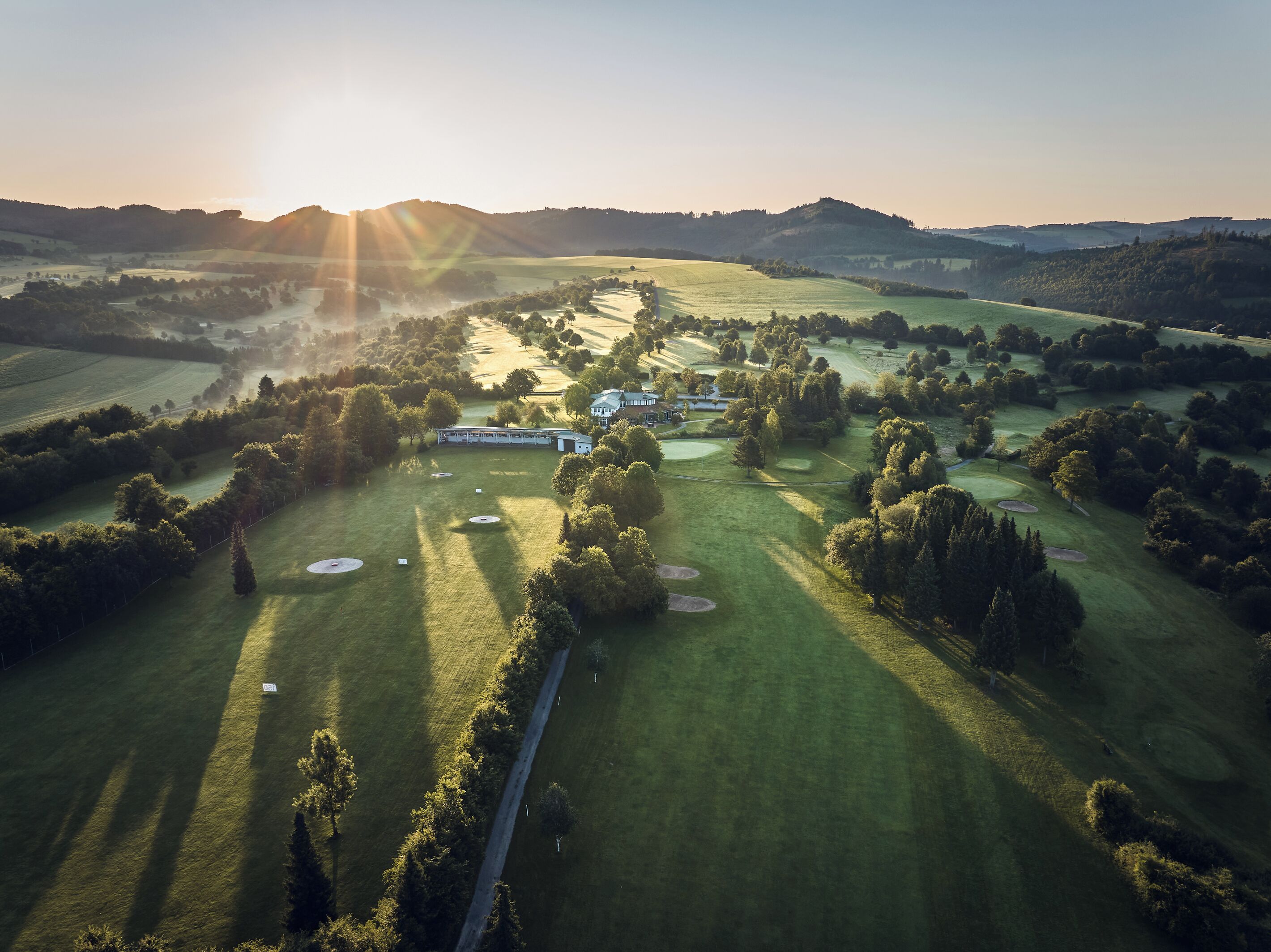 Oversigtsbillede af en golfbane med flere bunkers, et klubhus og omkringliggende marker.