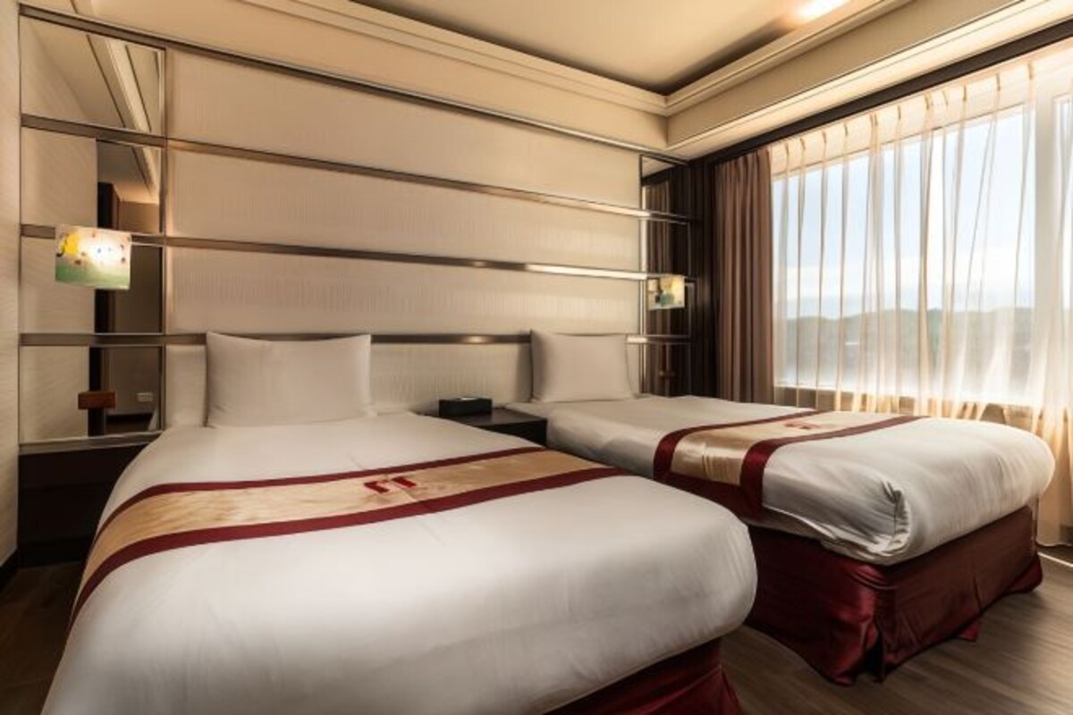 A hotel room with two beds, a large window with curtains, and a mirror on the wall.