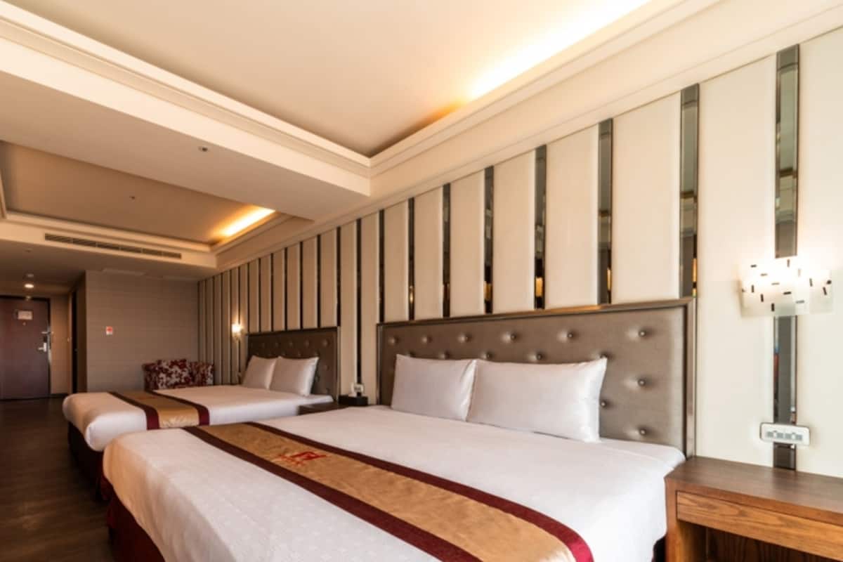 Ett hotellrum med två sängar, ett skrivbord i trä, en minibar och en väggmonterad lampa.