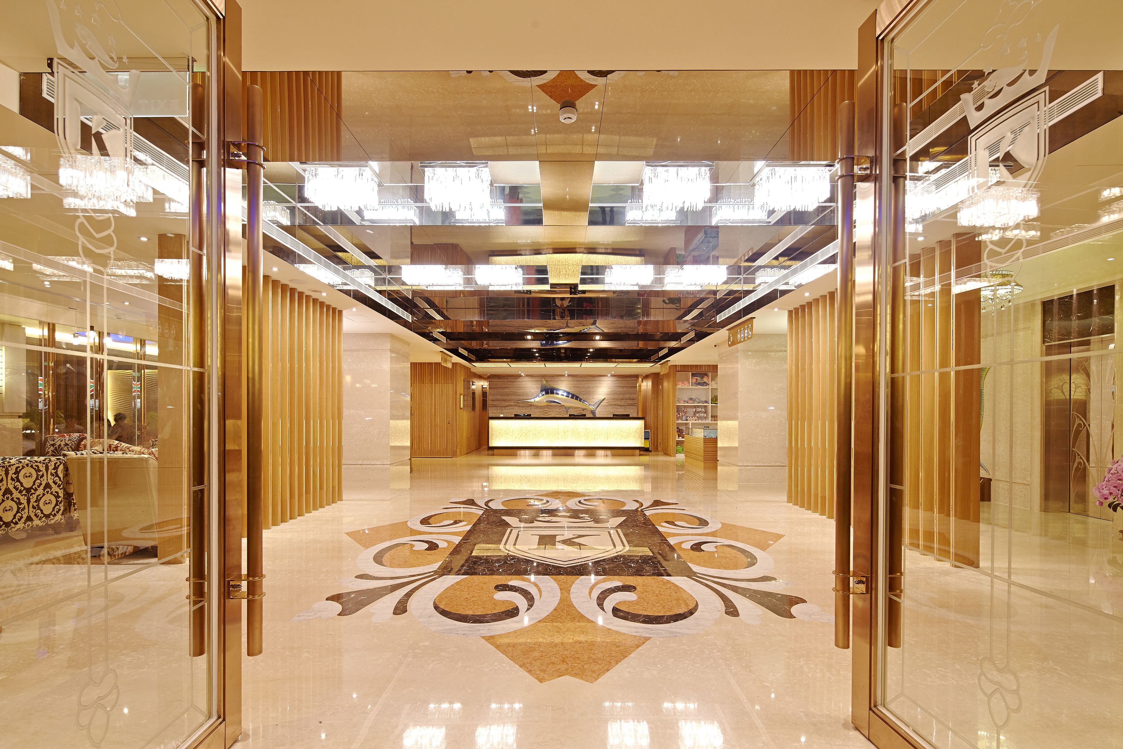 A hotel lobby with a reception desk, glass doors, and a decorative floor pattern.