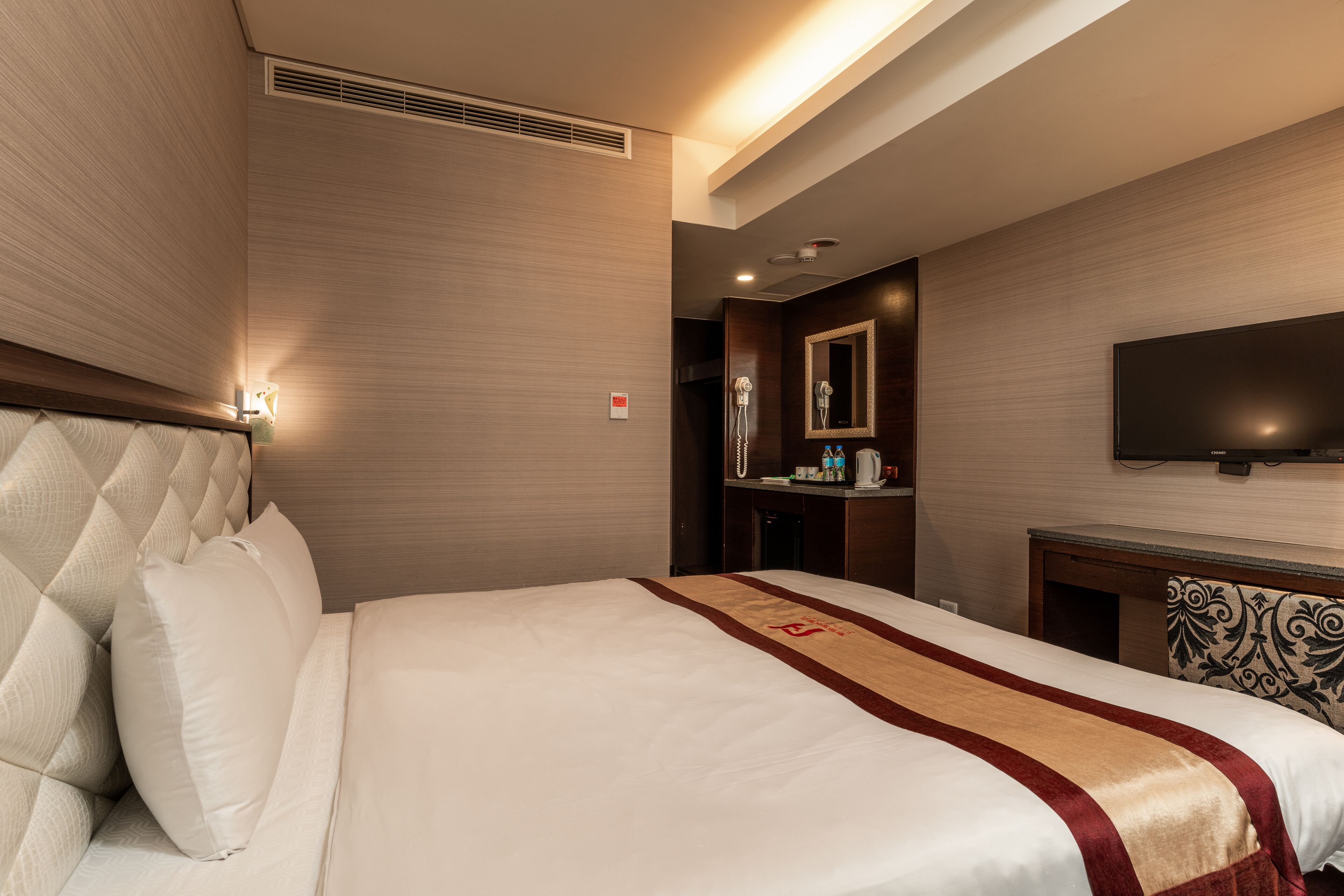 Een hotelkamer met een groot bed, een flatscreen televisie aan de muur, een bureau met een stoel en een spiegel boven het bureau.