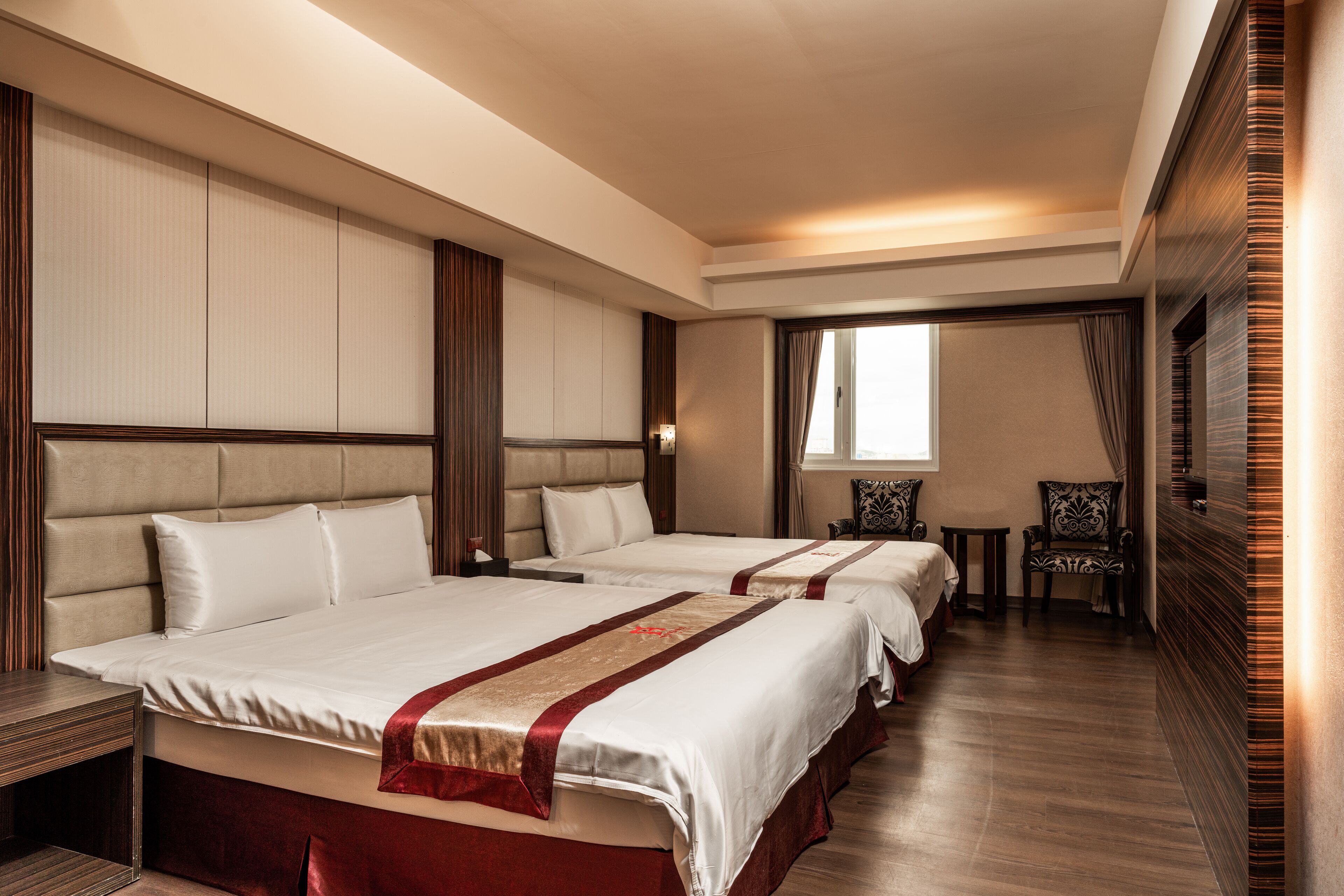 A hotel room with two beds, a small table, and a chair.