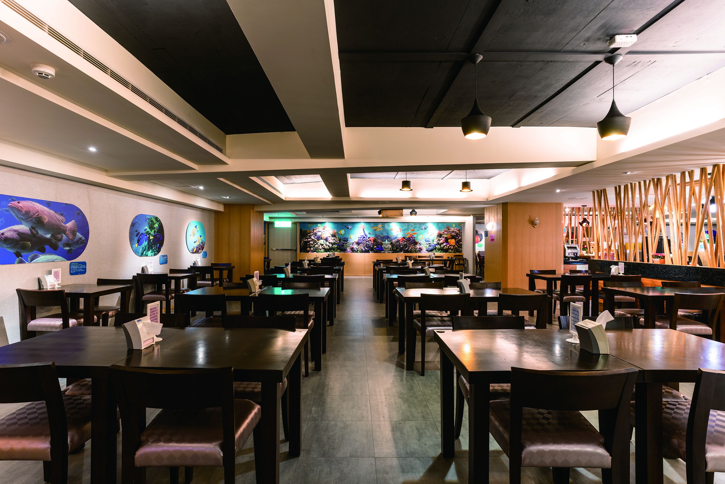 Un restaurant avec de nombreuses tables et chaises, un grand aquarium en arrière-plan et des lambris en bois sur un des murs.