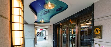Een hotelentree met een modern ontwerp, met een opvallend plafond in blauw- en groentinten en een centraal lichtarmatuur.