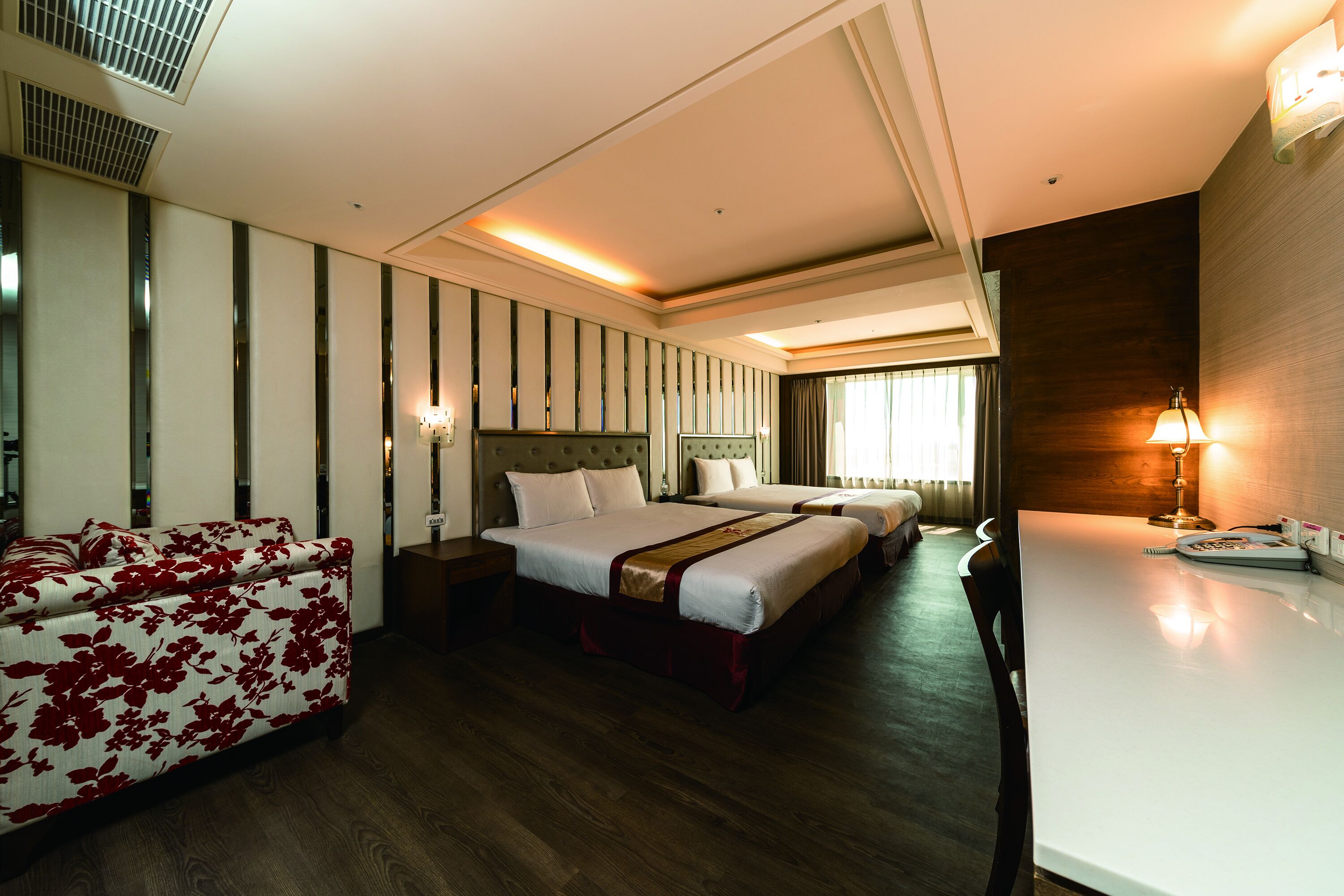 Une chambre d’hôtel avec un canapé, deux lits, un bureau et une lampe.
