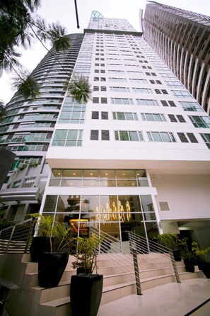 A modern building with a glass facade, multiple floors, and a staircase leading to the entrance. - Avant Apartments At The Fort (Taguig)
