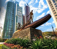 Una escultura de una figura con un objeto grande, frente a un fondo de modernos rascacielos.