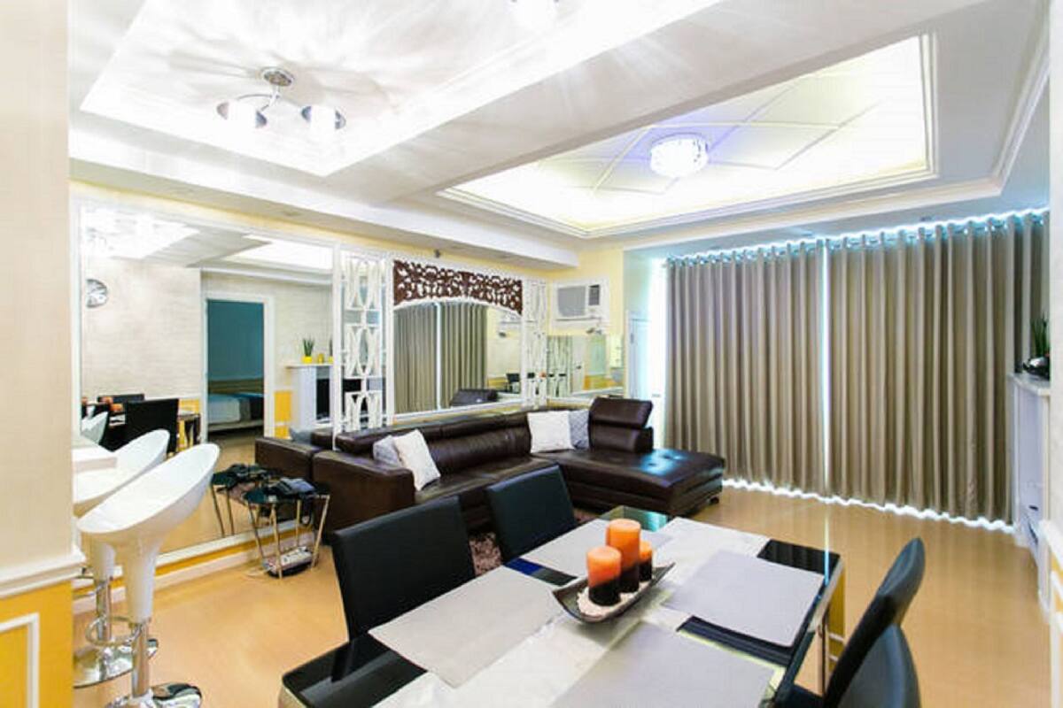 A modern living room with a dining area, a large window with curtains, and a ceiling with recessed lighting.